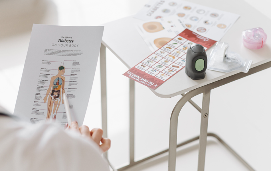 Person hält eine Infografik über die Auswirkungen von Diabetes auf den Körper, daneben liegt ein Blutzuckermessgerät.